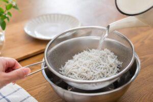 釜揚げしらすに熱湯をかけて湯通しする様子
